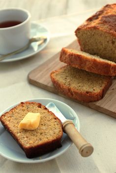 slices of banana bread with butter on a plate next to a cup of tea and spoon