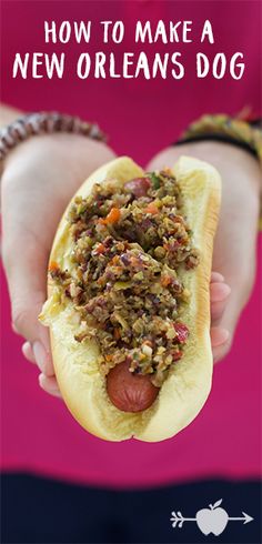 a person holding a hot dog with toppings on it in front of a pink background