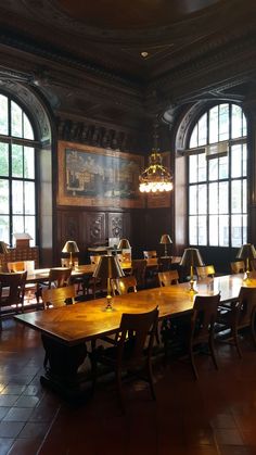 a large dining room with wooden tables and chairs in it, along with two chandeliers hanging from the ceiling