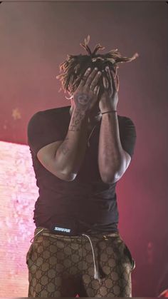 a man with dreadlocks covering his face while standing in front of a stage