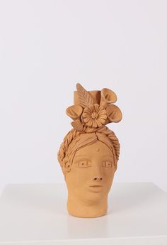 a clay sculpture of a woman's head with flowers in her hair on a white surface