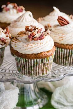 cupcakes with white frosting and pecans on top sitting on a glass plate