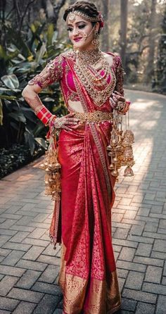 a woman in a red and gold sari standing on a brick walkway with her hands on her hips