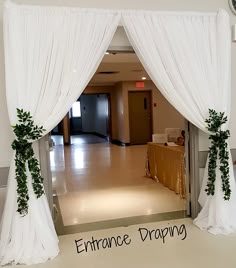 an entrance to a banquet hall decorated with white drapes and greenery