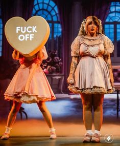 two women dressed in costumes and holding a heart shaped object with the words f k off written on it