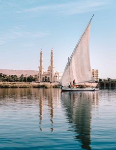 a sailboat sailing on the water in front of a large building