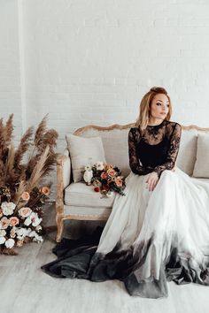 a woman sitting on a couch wearing a black and white wedding dress with sheer sleeves