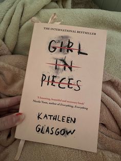 the book girl in pieces is being held up by someone's hand on a bed