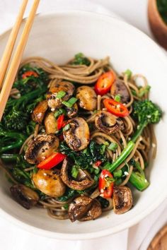 a white bowl filled with noodles, mushrooms and veggies next to chopsticks