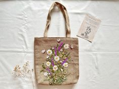 a small bag with flowers on it sitting next to a plant and an old book