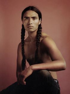 a woman with long braids sitting in front of a red wall and looking at the camera