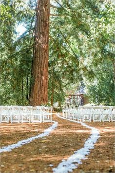 an outdoor ceremony set up with white chairs in front of a large tree and a gazebo