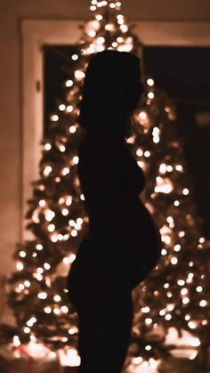 a pregnant woman standing in front of a lit christmas tree with her belly exposed and hands on her hips