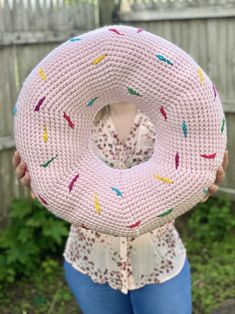 a woman holding up a knitted donut pillow