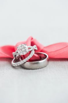 two wedding rings sitting on top of each other next to a pink satin bow and ribbon