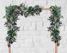 a wooden frame decorated with greenery on a white brick wall in the shape of an arch