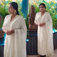 a woman wearing a white sari standing in front of a statue and looking off to the side