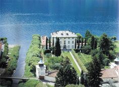 an aerial view of a large house in the middle of a lake with trees around it