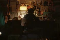 a person sitting at a desk in front of a lamp and pictures on the wall