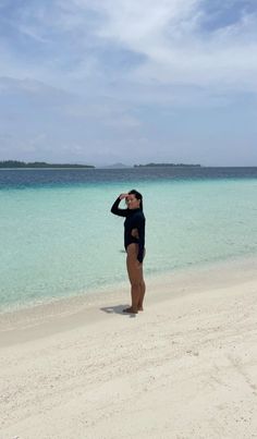 a woman standing on top of a sandy beach next to the ocean with clear blue water