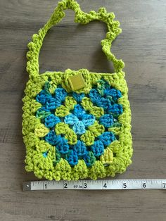 a crocheted purse sitting on top of a wooden table next to a ruler