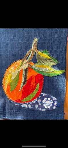 an orange painted on top of a blue piece of cloth with flowers and leaves around it