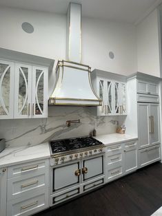 a kitchen with marble counter tops and white cabinets, gold trimming on the hood