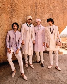 three men standing next to each other in front of a large rock with one man wearing a turban