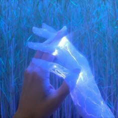 a hand is holding an ice - like object in front of some tall grass and blue lights