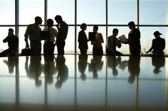 silhouettes of business people standing in front of a window with the sun shining through