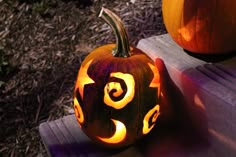 two carved pumpkins sitting next to each other on a wooden bench in the sun