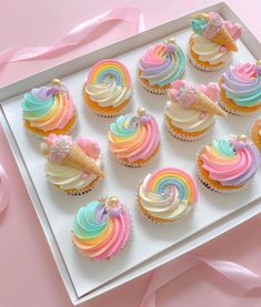 cupcakes decorated with rainbow icing and ice cream on a white tray next to pink ribbon