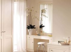 a bedroom with white furniture and flowers in vases on the vanity table next to it