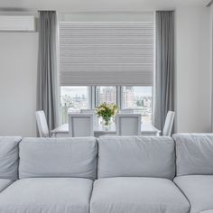 a living room filled with furniture and a window covered in shades of light grey curtains