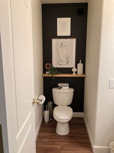 a white toilet sitting inside of a bathroom next to a wooden floor and wall mounted art