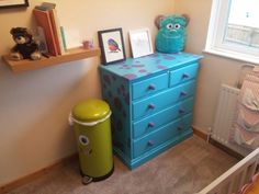 a child's room with a blue dresser and green trash can in the corner