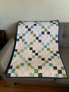 a green and white quilt sitting on top of a couch next to a gray chair