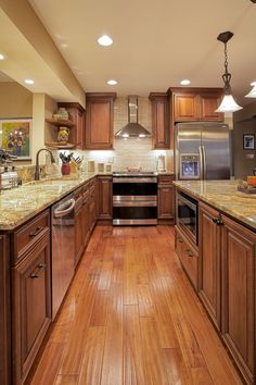 a large kitchen with wooden floors and stainless steel appliances, along with granite counter tops