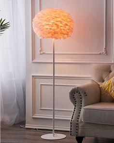 a white floor lamp sitting on top of a wooden table next to a chair and window