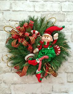 a christmas wreath hanging on a brick wall with an elf doll in the center and candy canes around it