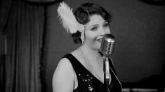 a woman with a feathered headband on singing into a microphone in a black and white photo