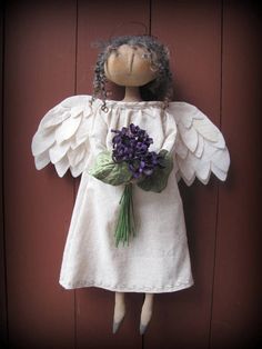 an angel doll with wings and flowers on it's head is posed against a red door