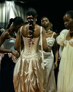 several women in dresses are standing together and looking at something on the floor behind them