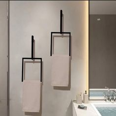 three towels hanging on the wall next to a bathtub in a room with white walls