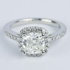 a cushion cut diamond ring with pave set diamonds around the band and halo setting