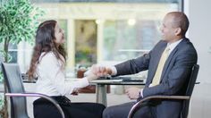 two people sitting at a table shaking hands in front of a plant and potted tree