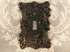 an ornate light switch plate is shown on a wallpapered background with white and gold damask