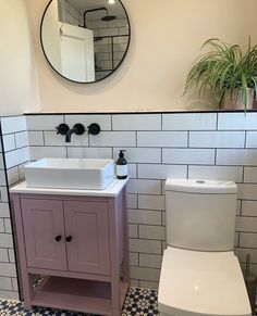 a white toilet sitting next to a sink in a bathroom under a round mirror on the wall