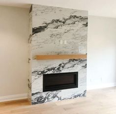 an empty living room with a fireplace and marbled wall in the corner, along with hard wood flooring