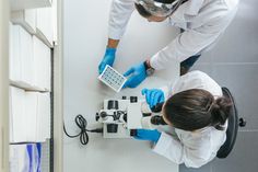 two people in white coats and blue gloves looking at microscopes